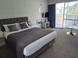 A hotel room with a large bed, a bedside table, a TV, and a balcony with a view. - Aaron Court Motel (Whangarei)