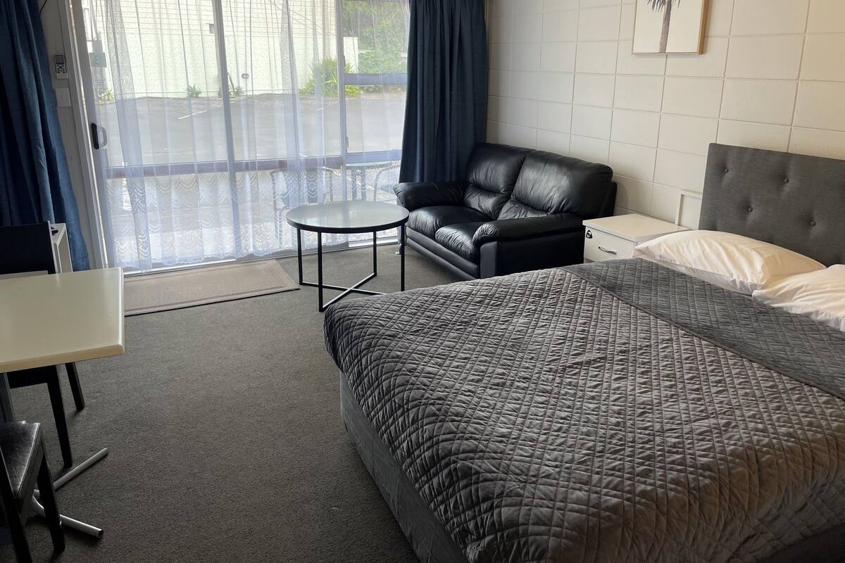Una habitación de hotel con cama, sofá, una mesita y ventana con cortinas.