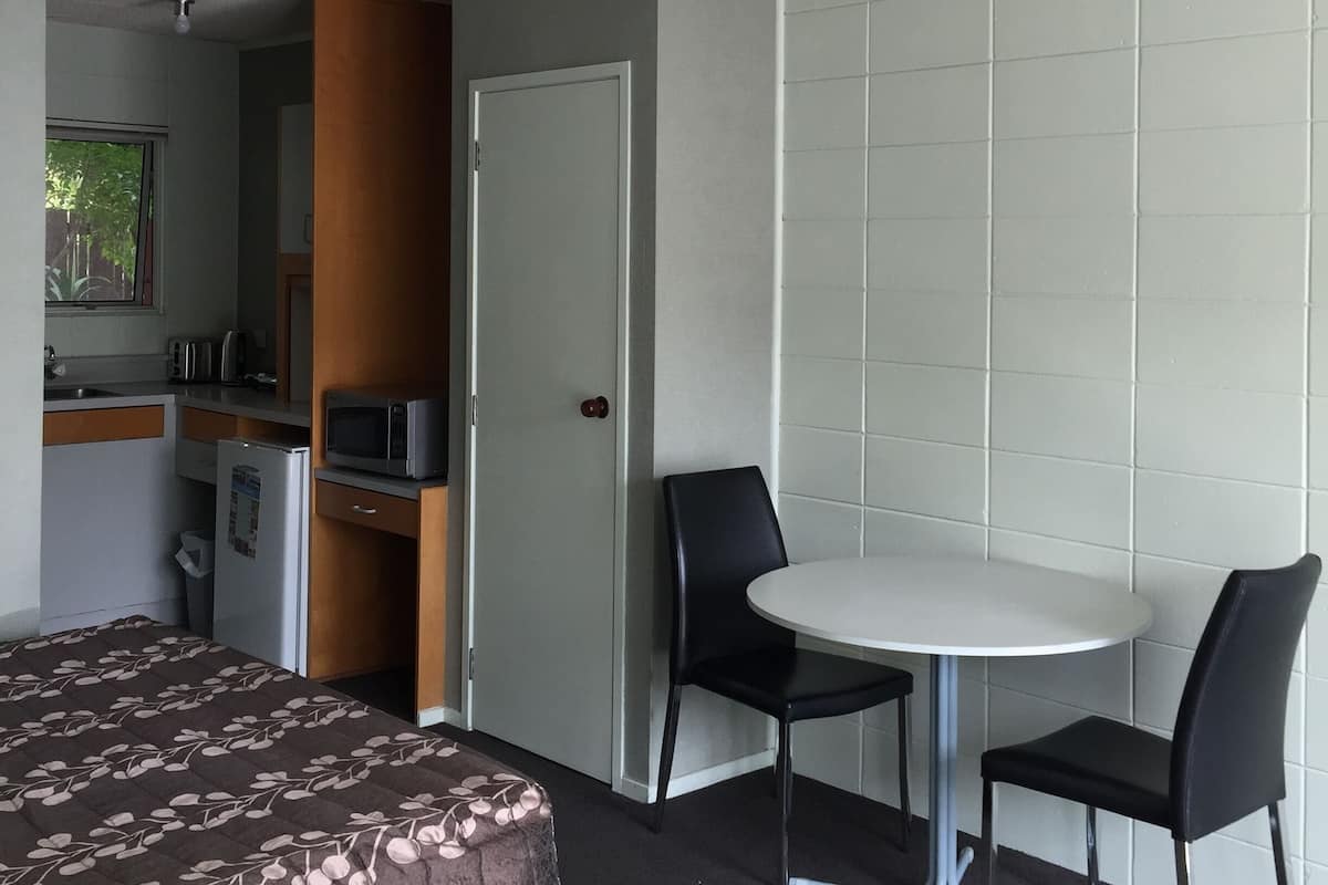 Una habitación de hotel con cama, una kitchenette pequeña, una mesa de comedor con sillas y una puerta que da a otra habitación.