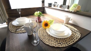 Ett matbord dukat med vita tallrikar, skålar och bestick, tillsammans med ett glas och en vas med blommor.