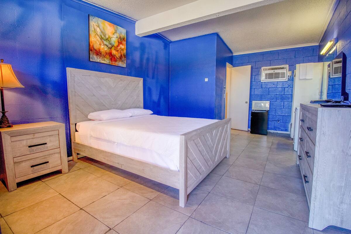A bedroom with a bed, a nightstand, a dresser, and a bathroom with a mirror and sink.