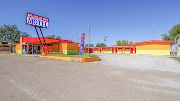 A motel with a red and yellow exterior, a clear blue sky, and a sign reading "Wheeler Inn Motel".
