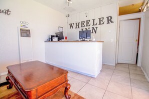 A hotel reception desk with a sign reading 'WHEELER INN,' a small desk with a computer and a telephone, and a wooden table in the foreground. - Wheeler Inn Texas, Us - 83 By OYO (Portland)