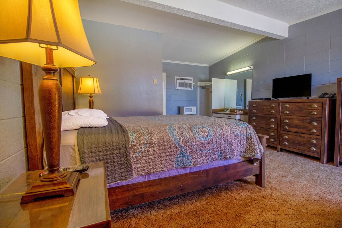 A bedroom with a bed, a dresser, a television, and a lamp.