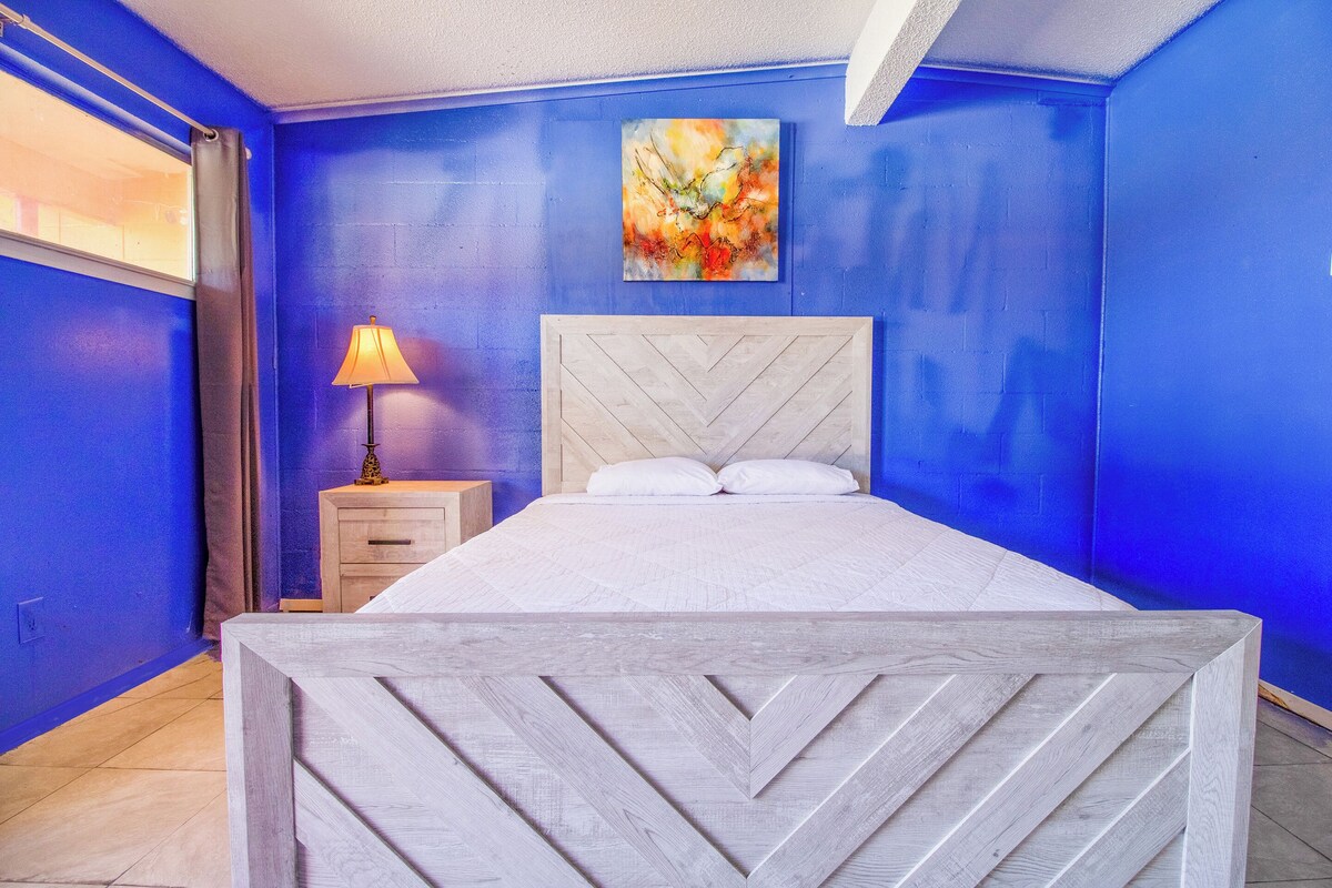 A bedroom with a bed, a nightstand, a lamp, and a painting on the wall.