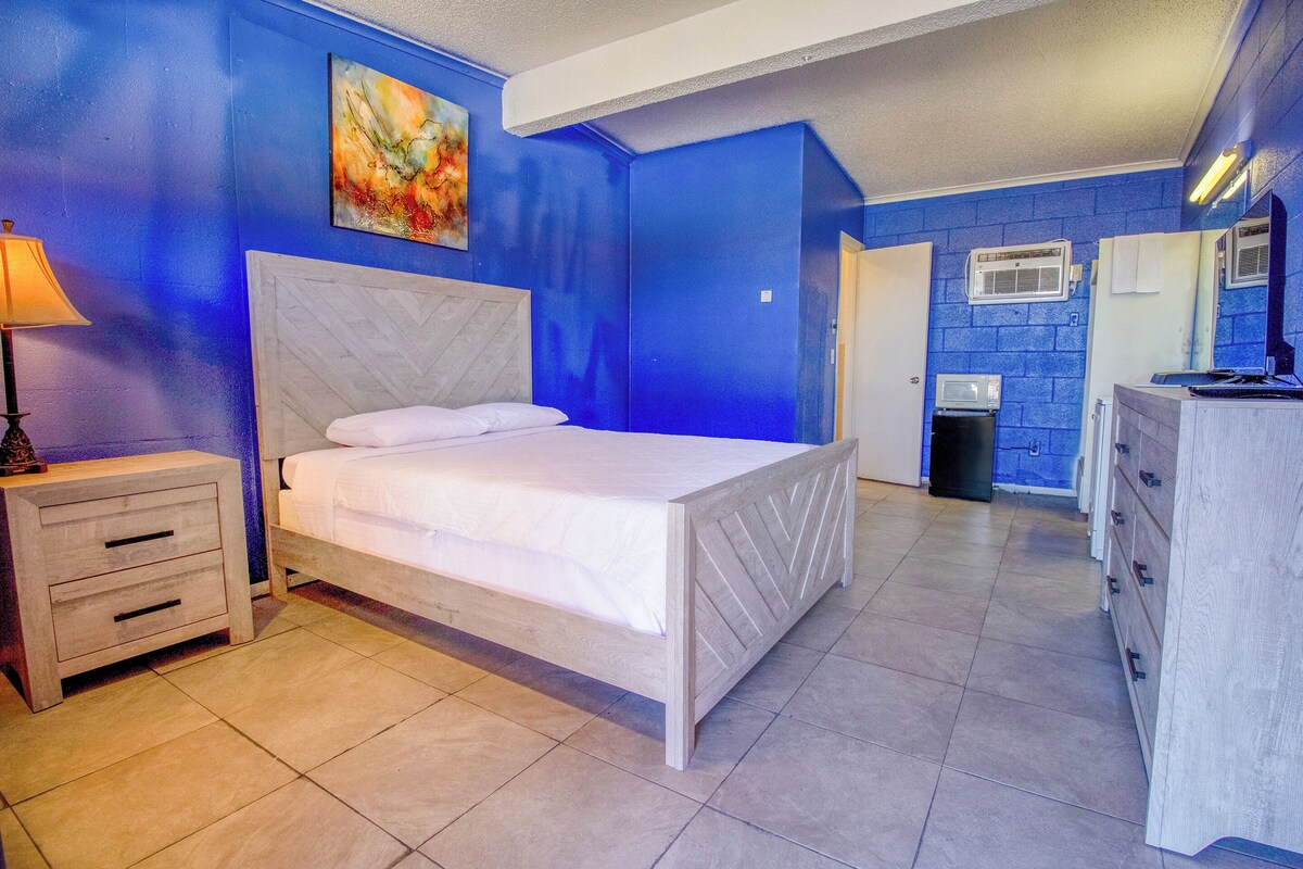 A bedroom with a bed, a nightstand, a dresser, and a bathroom with a mirror and sink.