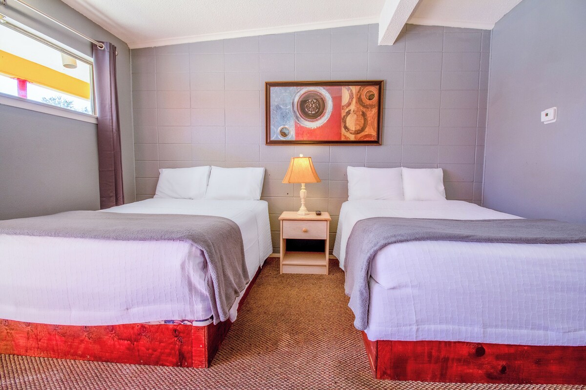 Una camera d'albergo con due letti, un comodino con una lampada e un quadro appeso al muro.