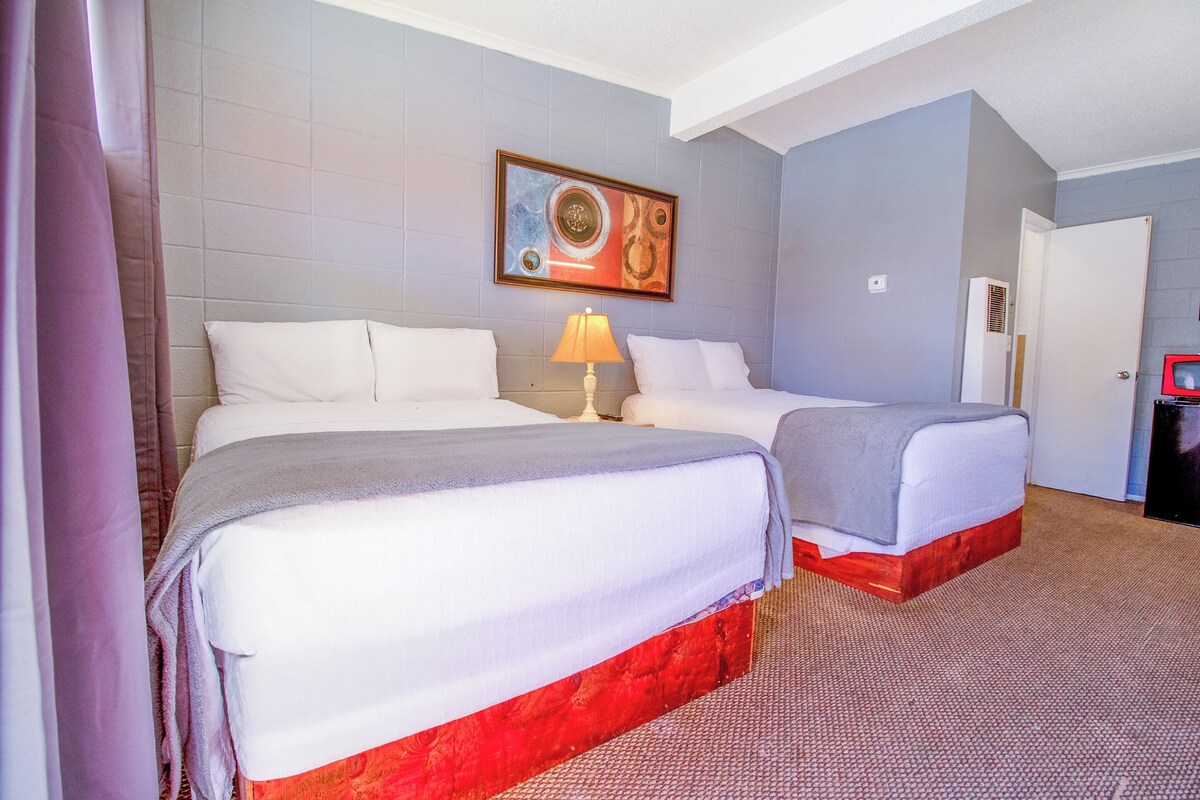A hotel room with two beds, a painting on the wall, and a red carpet.