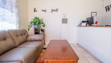 A living room with a brown leather sofa, a wooden coffee table, a potted plant, and a sign that reads "be our guest."