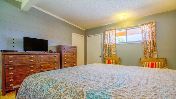 A bedroom with a large bed, a dresser with multiple drawers, a television on top, and a window with patterned curtains.