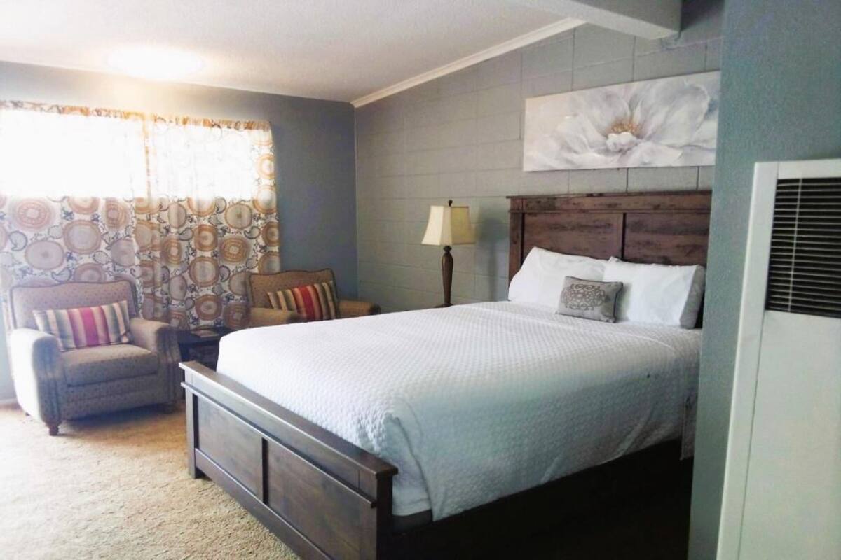 A bedroom with a bed, chair, lamp, and a wall-mounted air conditioning unit.