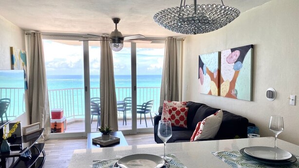 A modern living room with a view of the ocean, a dining area with a glass table, and a cozy seating area with a sofa and cushions.