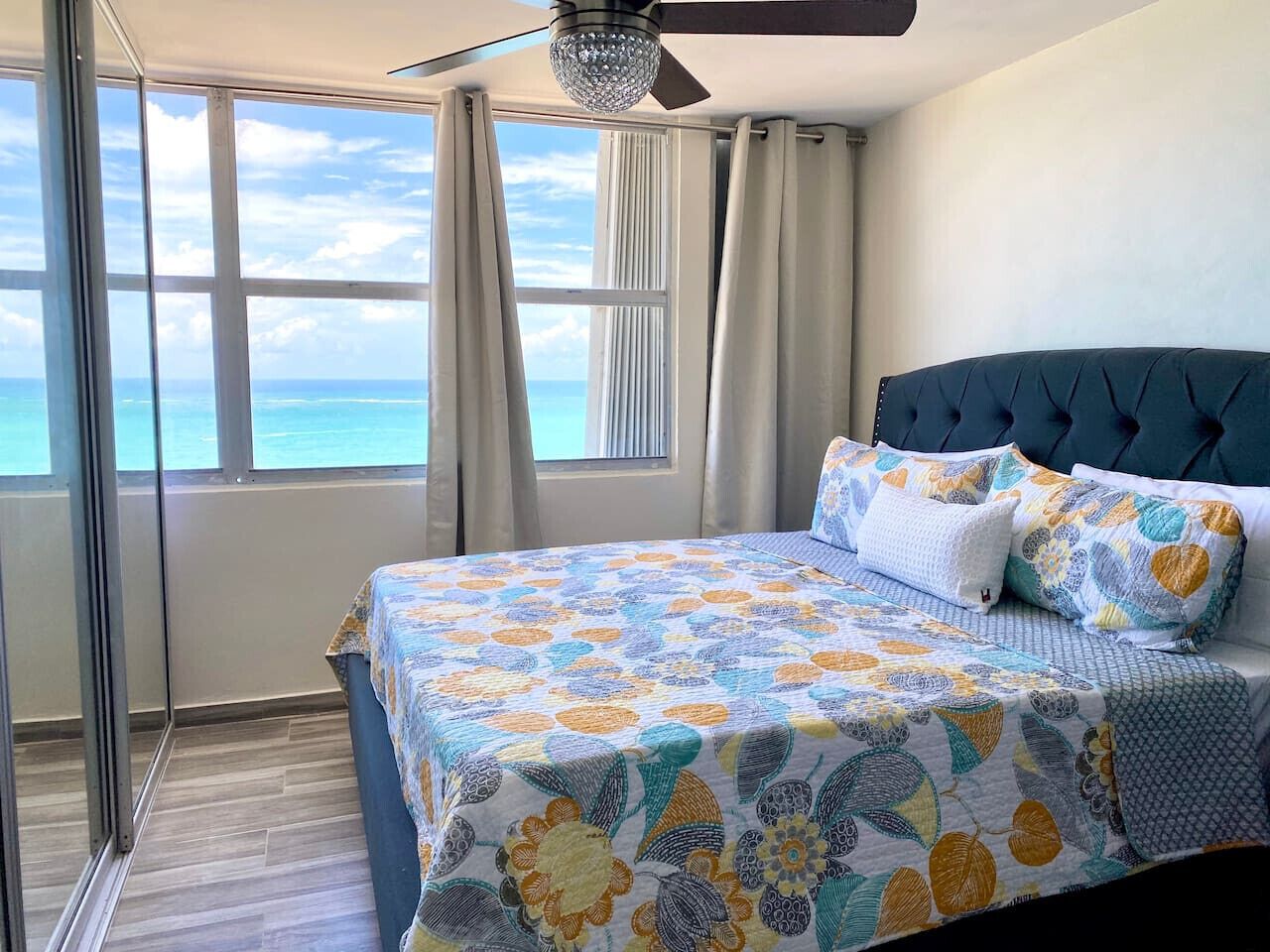 Een slaapkamer met een groot bed, uitzicht op de oceaan en een plafondventilator.