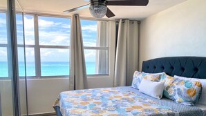 A bedroom with a large bed, a view of the ocean, and a ceiling fan.