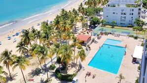 A beachside hotel with a swimming pool, palm trees, and a view of the ocean.