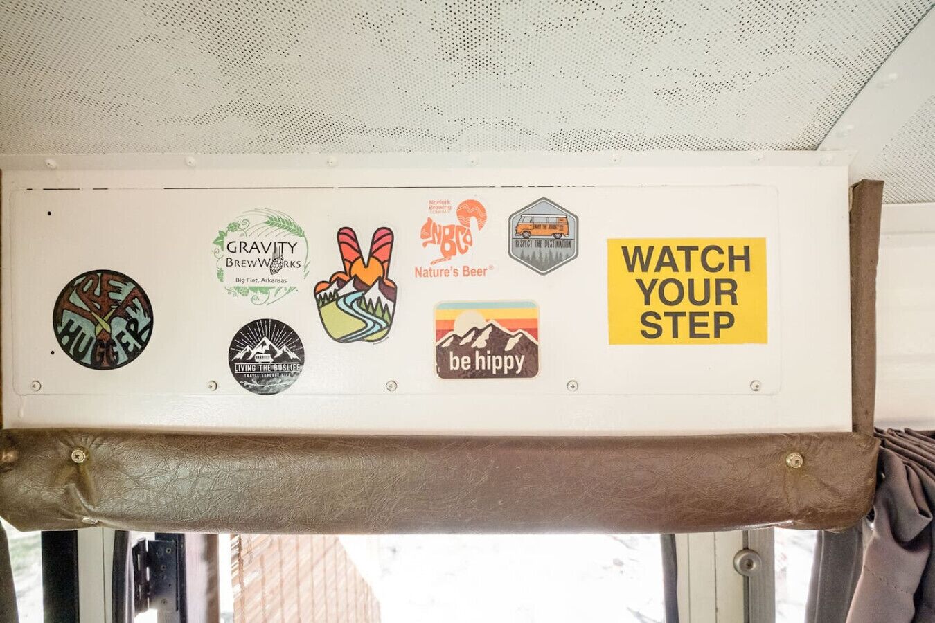 Una pared con varios adhesivos, incluyendo logotipos y frases como "Gravity Brewworks", "Nature's Beer" y "Be Hippy".