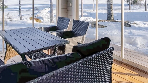 A sunroom with a view of a snowy landscape, furnished with wicker chairs and a table. - Suvituuli by Interhome (Pertunmaa)