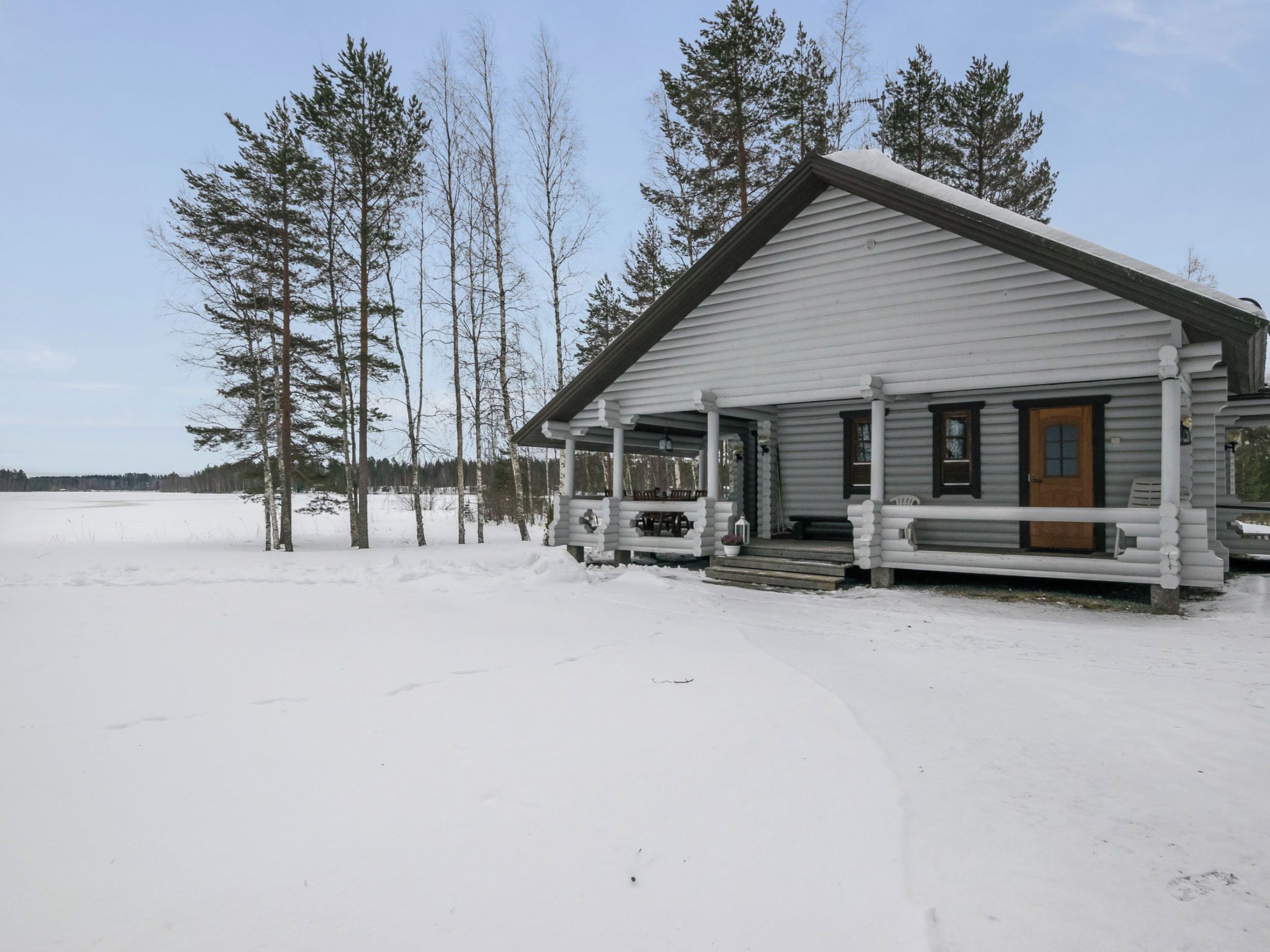 A log cabin with a porch and a front door, surrounded by snow and trees.