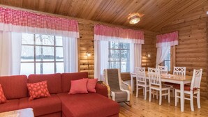 A cozy cabin interior with a red sectional sofa, a dining table with white chairs, and wooden walls. - Suvituuli by Interhome (Pertunmaa)