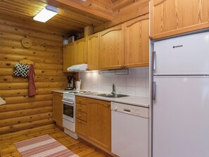 A compact kitchen with wooden cabinets, a white refrigerator, a stove, and a dishwasher. - Suvituuli by Interhome (Pertunmaa)