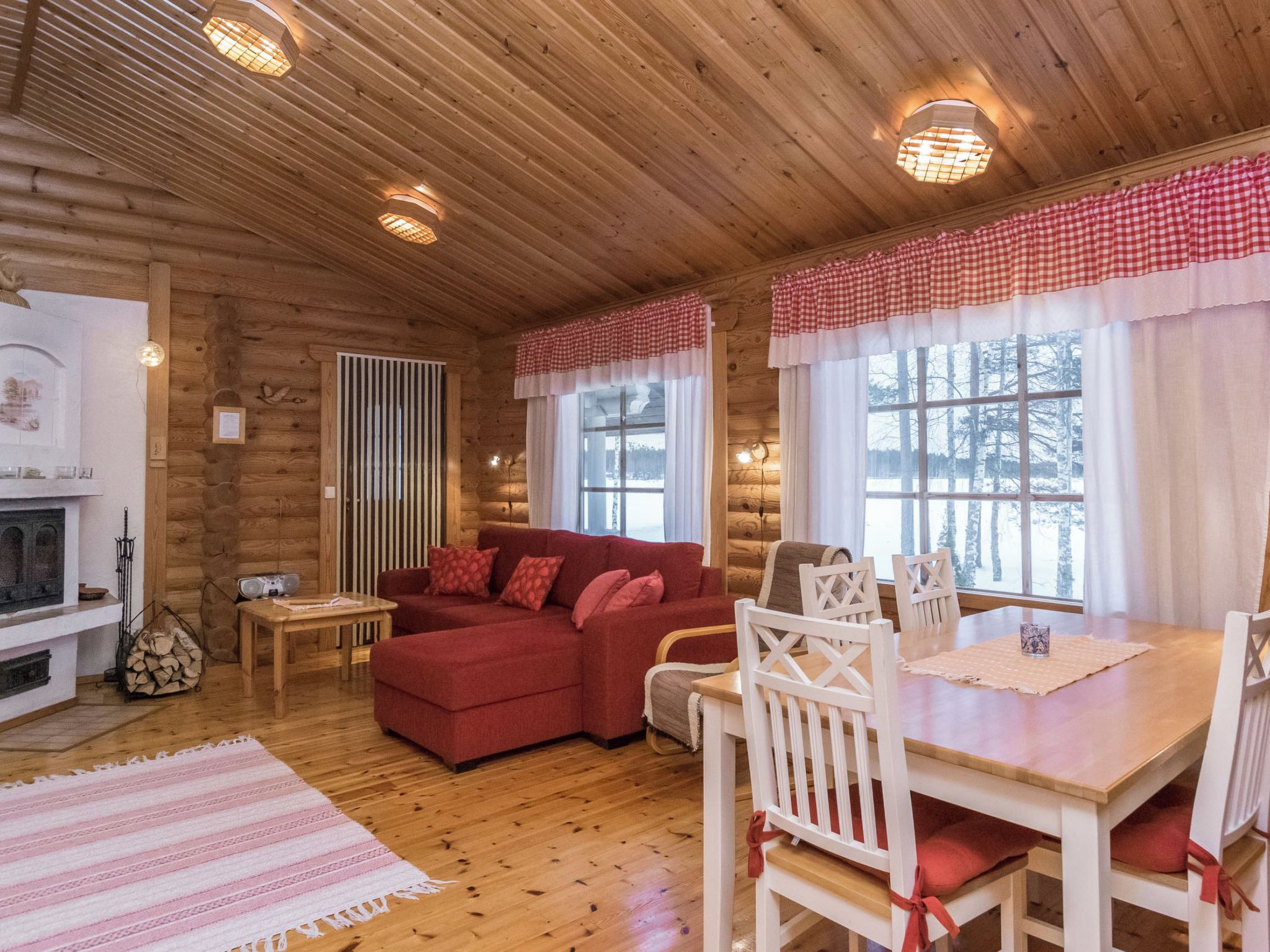 L’intérieur d’un chalet confortable, avec un canapé rouge, des chaises blanches, une table à manger et une cheminée.