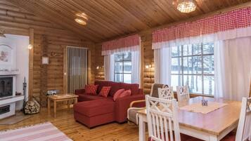 L’intérieur d’un chalet confortable, avec un canapé rouge, des chaises blanches, une table à manger et une cheminée.