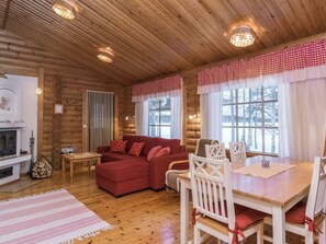 A cozy log cabin interior with a red sofa, white chairs, a dining table, and a fireplace. - Suvituuli by Interhome (Pertunmaa)