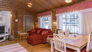 A cozy log cabin interior with a red sofa, white chairs, a wooden dining table, and a fireplace. - Suvituuli by Interhome (Pertunmaa)