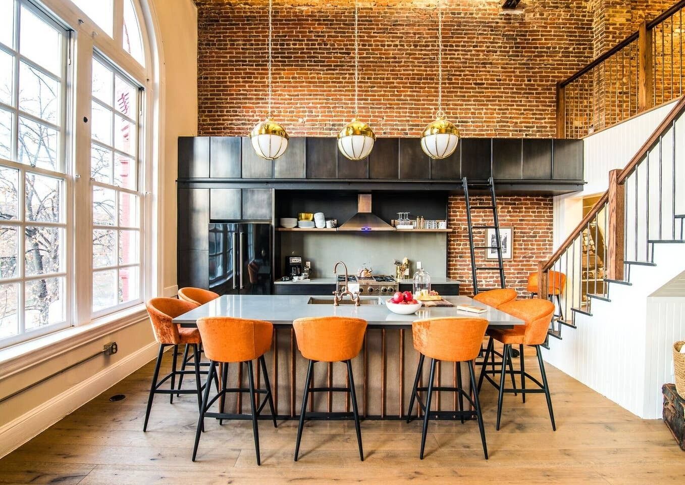 Une cuisine moderne avec un mur en briques, un grand îlot central doté de tabourets et des luminaires suspendus.