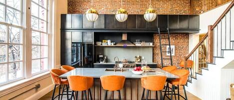 Une cuisine moderne avec un mur en briques, un grand îlot central doté de tabourets et des luminaires suspendus.