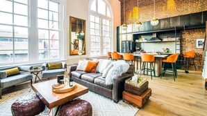 A spacious living room with a leather sofa, a dining area with orange chairs, and a kitchen with a brick wall. - Historic DC Firehouse Penthouse Loft (Washington)