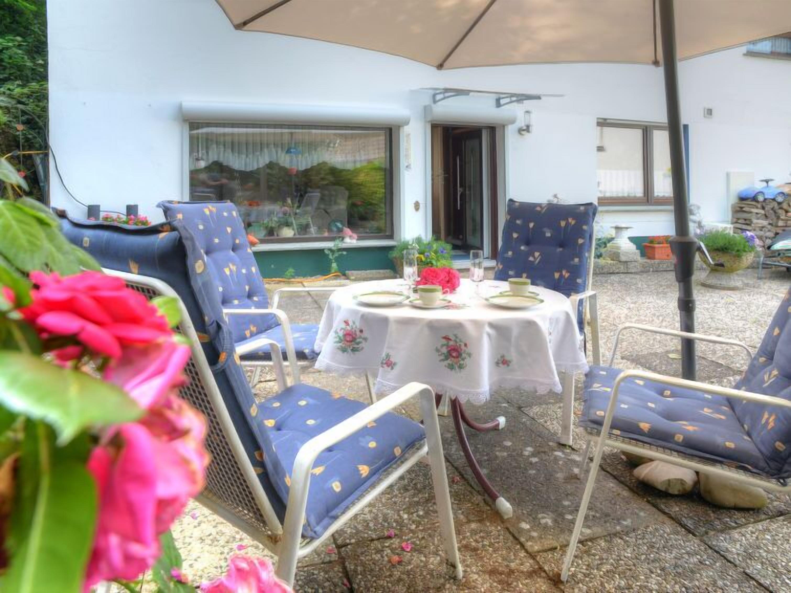 Un patio al aire libre con una mesa redonda y cuatro sillas, un paraguas blanco y un edificio blanco al fondo.