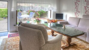 A living room with a sofa, a chair, a coffee table, and a television. There is a window with curtains, a door, and a view of a garden outside. - Am Dohlenberg by Interhome (Schwalenberg)