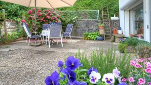 An outdoor patio area with a table and chairs under a large umbrella, surrounded by flowering plants and a stone wall. - Am Dohlenberg by Interhome (Schwalenberg)