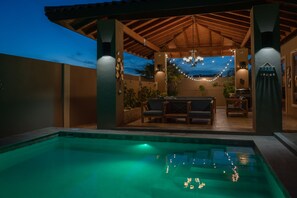 A pool area with a covered patio, seating, and string lights.