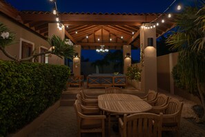 Une terrasse extérieure avec des meubles en bois, des guirlandes lumineuses et une pergola.