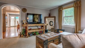 A cozy living room with a television, a fireplace, and a large window with curtains. - Wescott House in the historic Willamette District (West Linn)