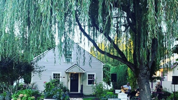 A house with a stone pathway leading to the front door, surrounded by lush greenery and a large tree with hanging branches. - Wescott House in the historic Willamette District (West Linn)