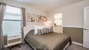 Um quarto com cama, mesa de cabeceira, janela com cortinas e decoração nas paredes.