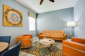 A retro-styled living room with a blue wall, orange furniture, and a patterned rug.