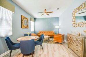 A modern living room with a blue sofa, a round dining table with blue chairs, a ceiling fan, and a decorative mirror.