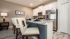 A modern kitchen with white cabinets, stainless steel appliances, and a marble countertop. - Champions Gate Golf Course Resort Town Home W/pool (Davenport)