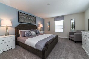 Un dormitorio con una cama grande, dos mesitas de noche, una silla, un aparador y una ventana con persianas.