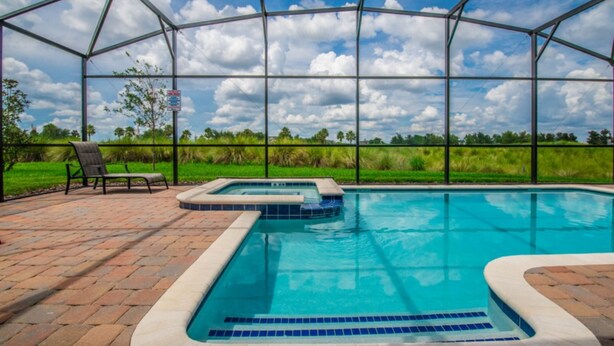 A covered swimming pool with a hot tub, surrounded by a brick patio and a metal fence. - Caddy Way Villa Chamapions Gate (Davenport)