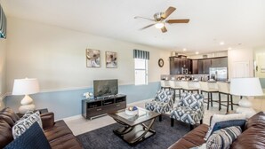 A living room with a brown leather sofa, a coffee table, and a TV. There is a kitchen area with a bar and counter. - Caddy Way Villa Chamapions Gate (Davenport)