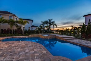A swimming pool with a brick patio, surrounded by palm trees and houses. - Golden Bear Villa Reunion (Kissimmee)
