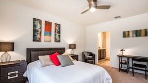 Une chambre avec un grand lit, un bureau, une chaise et des œuvres d’art accrochées aux murs.