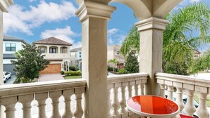 Een balkon met een rode stoel, uitzicht op een woonwijk en een heldere lucht.