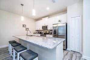 Una cocina moderna con armarios blancos, encimera de granito, electrodomésticos de acero inoxidable y taburetes de bar.
