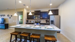A modern kitchen with a central island, dark cabinetry, stainless steel appliances, and pendant lighting.